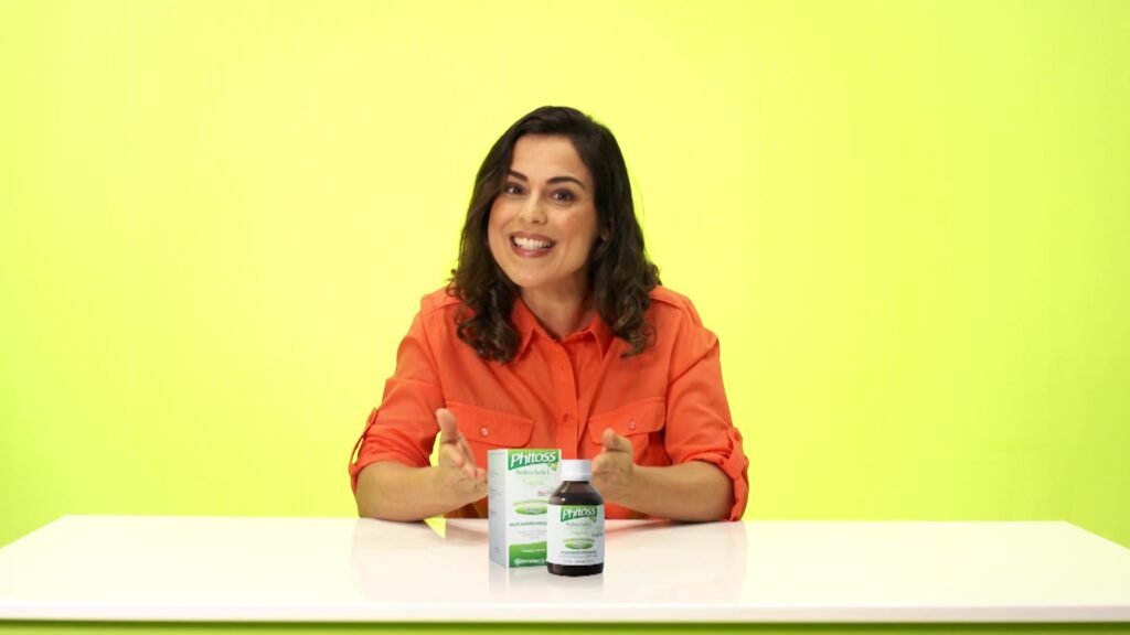 Presenter holding the product on a bright green set in a frame from the campaign film.